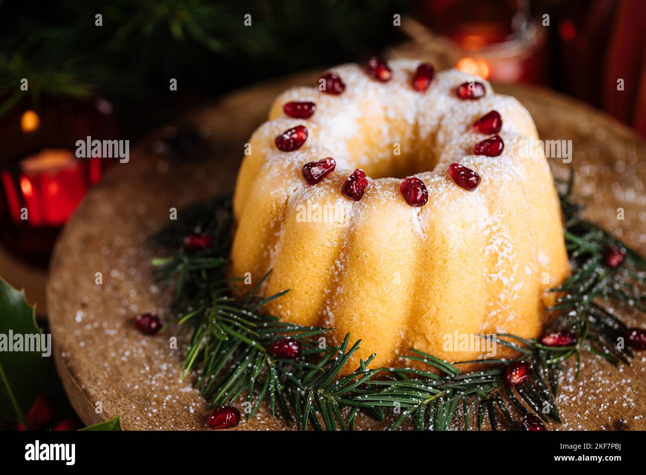 Gebüngelter Kuchen mit Zuckerzuckerung und Granatapfel in Weihnachtsstimmung. Stimmungsvolle Atmosphäre mit Kerzen und Dekoration. Silvester. Nachtisch genannt Stockfoto