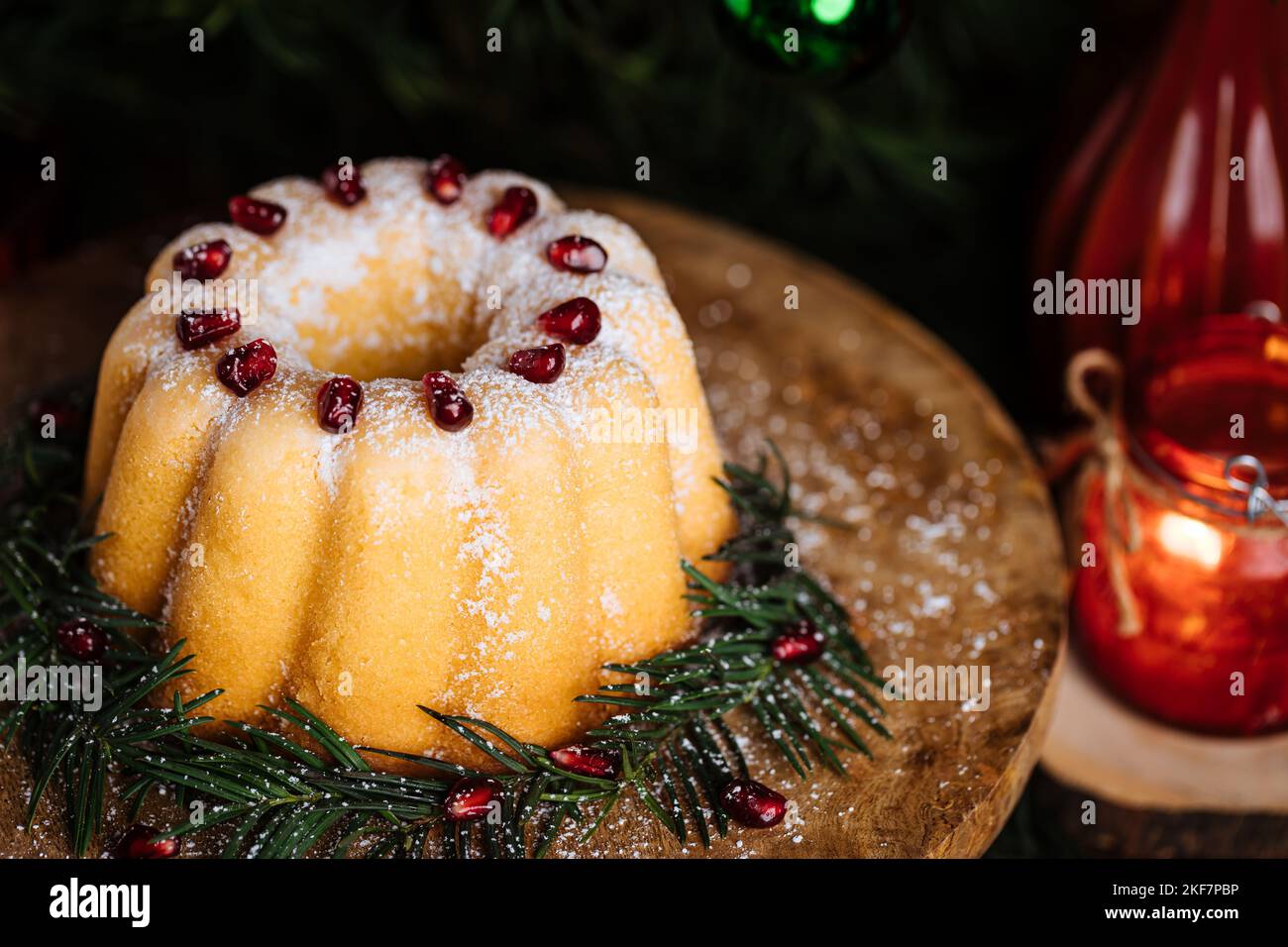 Gebüngelter Kuchen mit Zuckerzuckerung und Granatapfel in Weihnachtsstimmung. Stimmungsvolle Atmosphäre mit Kerzen und Dekoration. Silvester. Nachtisch genannt Stockfoto