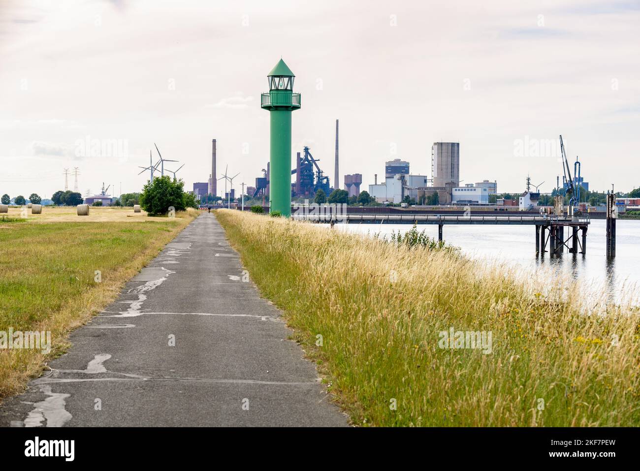 Leuchtturm auf einem asphaltierten Weg am Ufer der Weser in Bremen. Industrieanlagen und Lager sind im Hintergrund sichtbar. Stockfoto