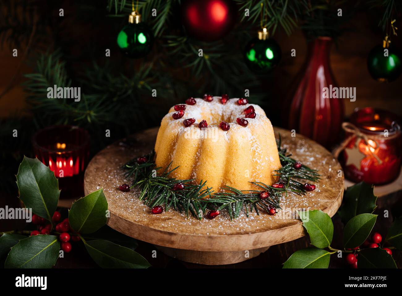 Gebüngelter Kuchen mit Zuckerzuckerung und Granatapfel in Weihnachtsstimmung. Stimmungsvolle Atmosphäre mit Kerzen und Dekoration. Silvester. Nachtisch genannt Stockfoto