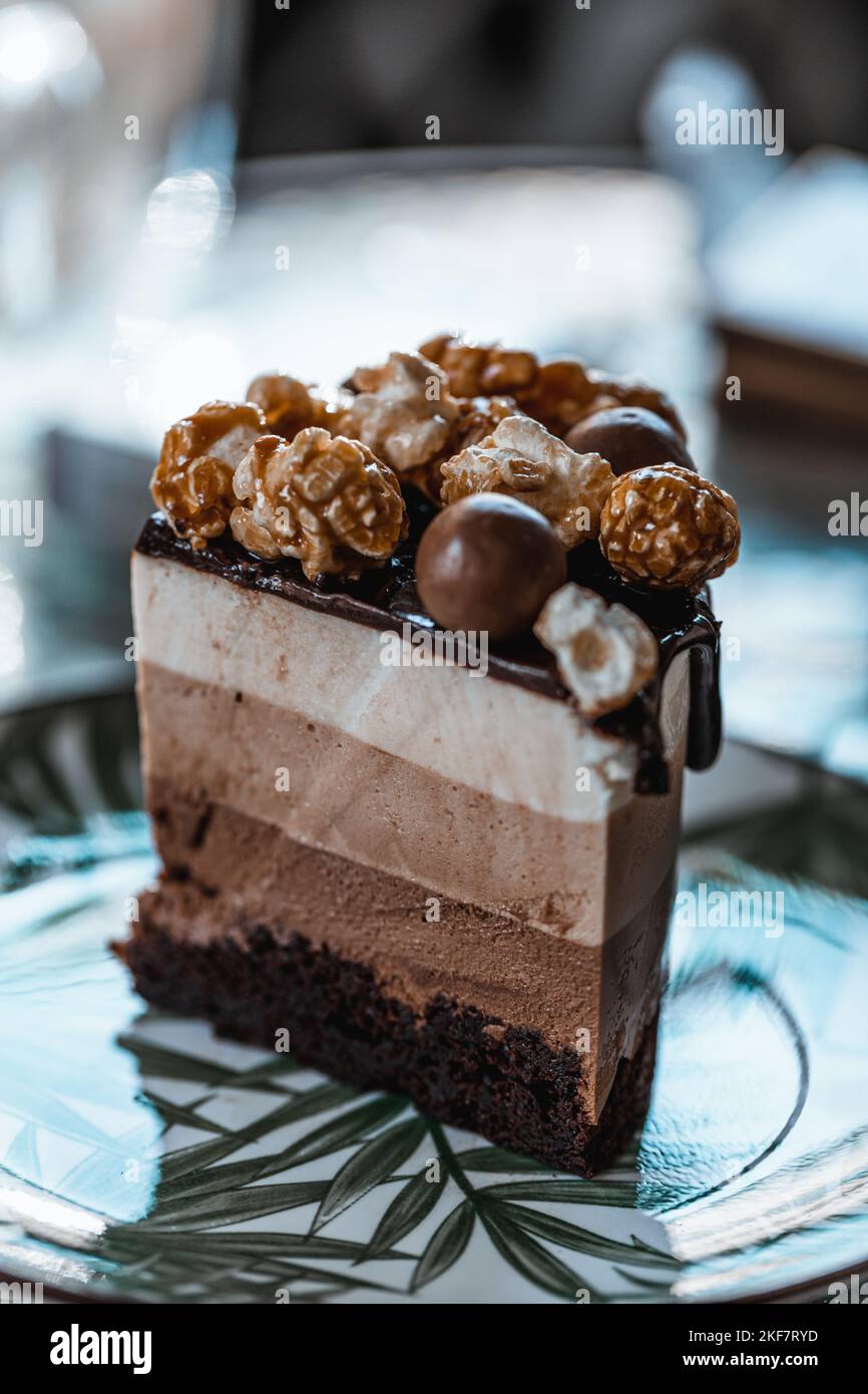Eine vertikale Aufnahme eines vierlagigen Schokoladenkuchenstückes, das mit Schokolade und Karamell-Popcorn verziert ist Stockfoto