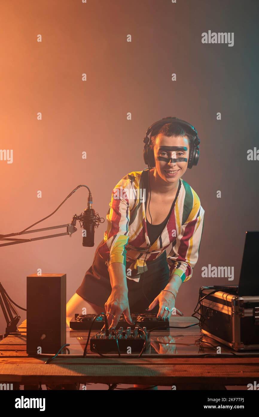 Lächelnde Frau dj, die Klänge an Plattenspielern mischt und Techno-Musik mit einem Audioinstrument und Geräten spielt. Fröhlicher Musiker mit verrückten Make-up mit Elektronik, um musikalische Leistung zu tun. Stockfoto