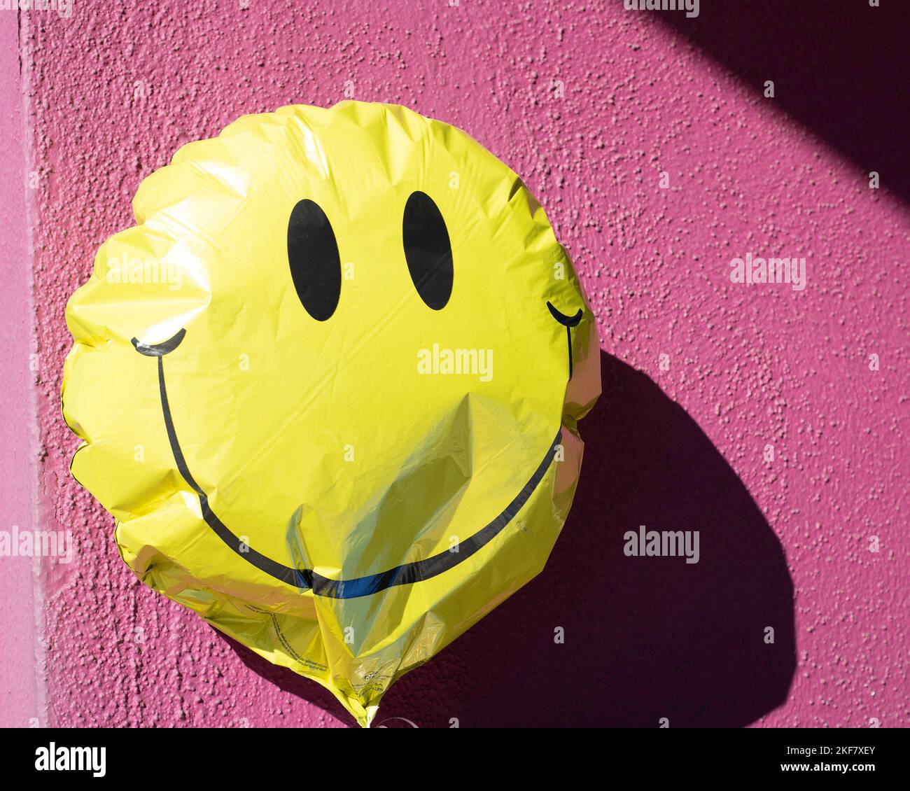 Nahaufnahme eines leuchtend gelben Mylar-Ballons mit fröhlichen Gesichten an einer rosa Wand. Stockfoto