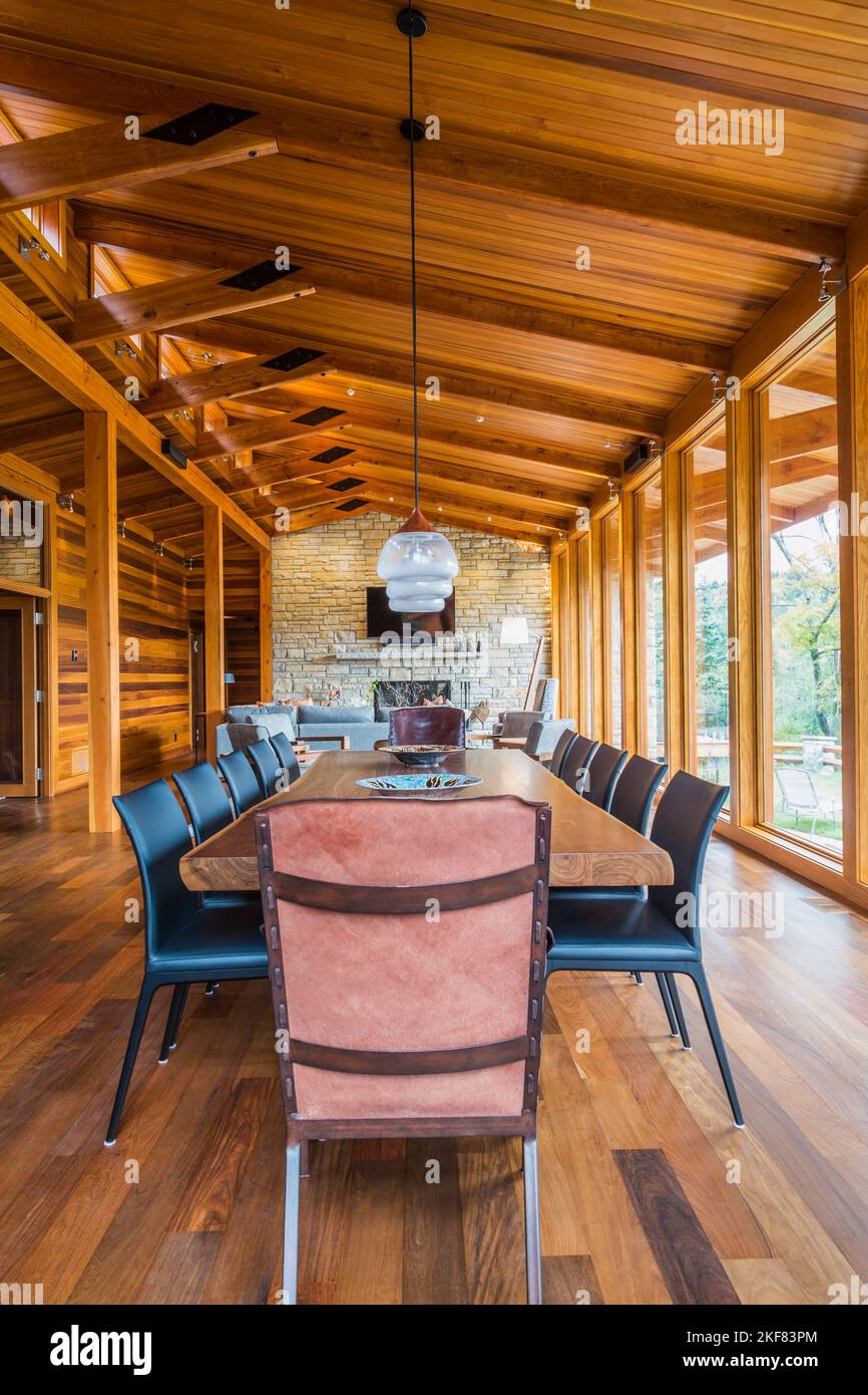 Esstisch aus Holz mit Ledersesseln, schwarzen Ledersesseln und Kupfer im industriellen Stil mit Hängeleuchten aus Milchglas. Stockfoto