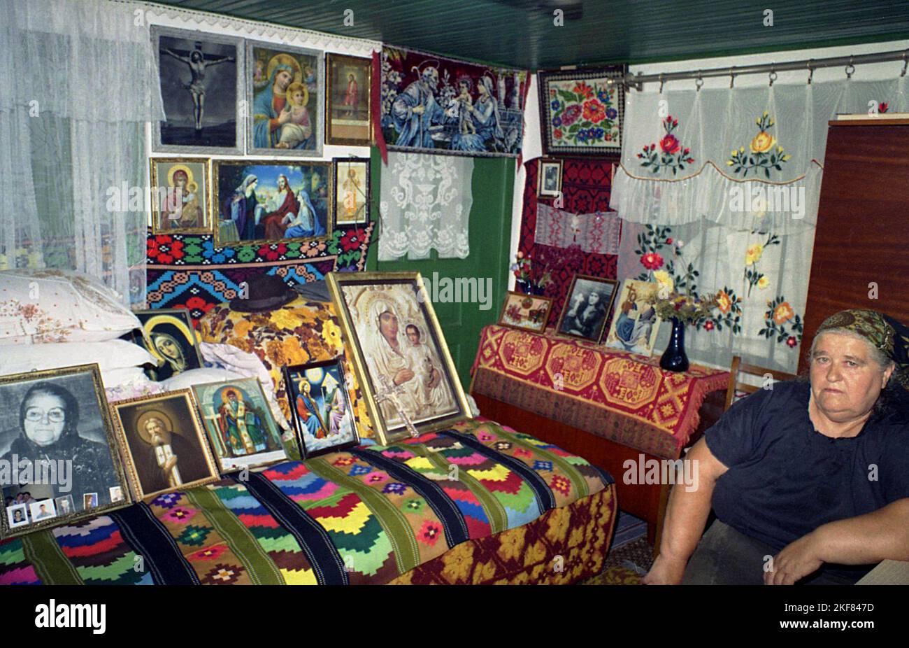 Ilfov County, Rumänien, ca. 2000. Frau in ihrem alten traditionellen Haus, mit einfachen Möbeln, handgefertigten Teppichen und einer Sammlung christlich-orthodoxer Ikonen. Stockfoto