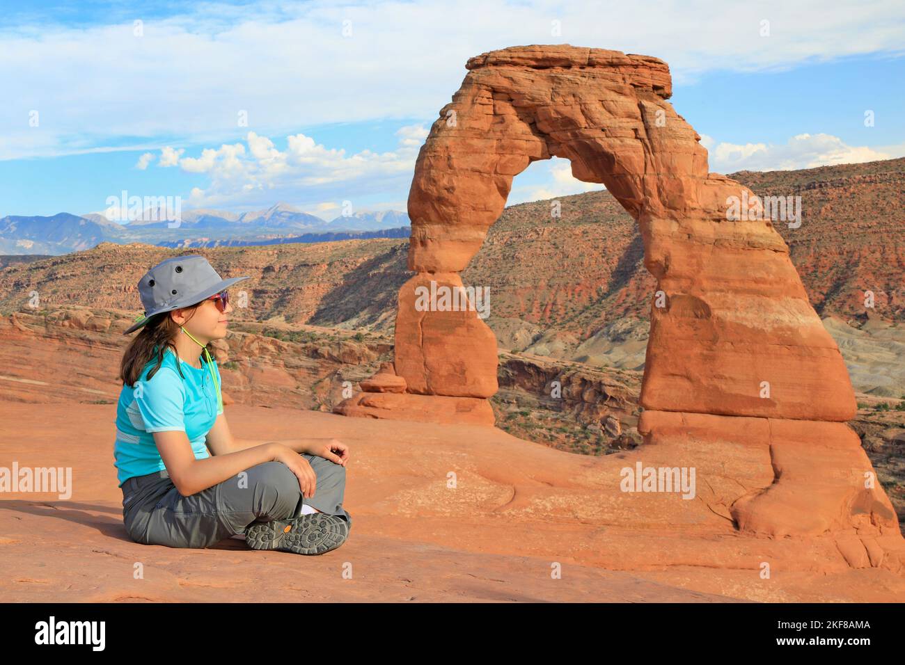 Junges Touristenmädchen, das bei Sonnenuntergang vor Delicate Arch in Utah, USA, sitzt Stockfoto