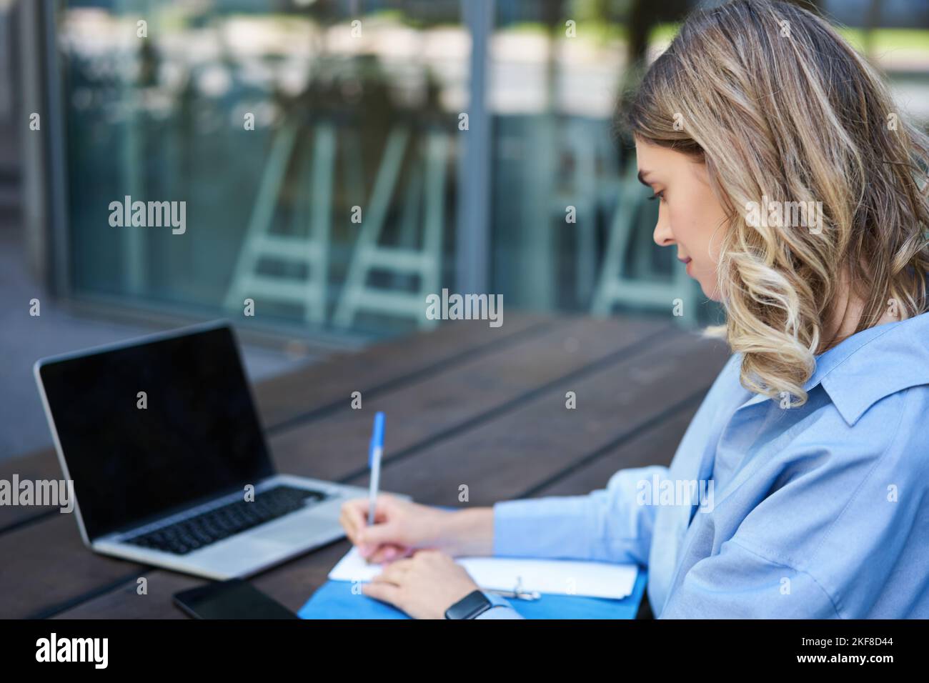 Nahaufnahme eines Porträts einer Studentin, die an Online-Kursen teilnimmt, mit einem Laptop an der frischen Luft sitzt und sich Notizen macht. Videochat für Geschäftsfrau Stockfoto