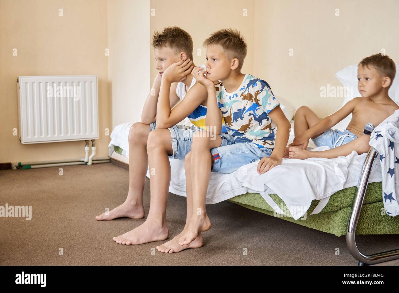 Geschwister, die auf einem Doppelbett sitzen, sehen gemeinsam Filme im fernsehen. Teenager und Vorschulkinder genießen es, gemeinsam im Hotel Fernsehen zu sehen und die Sommerferien zu verbringen Stockfoto