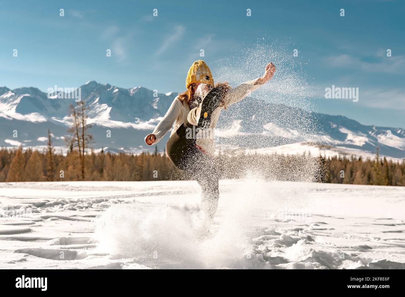 Happy girl in Pullover und Strickmütze hat Spaß und tritt Schnee in den Bergen Stockfoto
