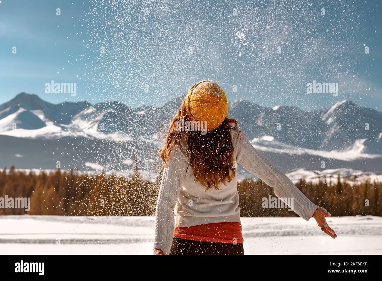 Glückliches Mädchen in Pullover und Strickmütze wirft Schnee in den Bergen und Spaß haben Stockfoto