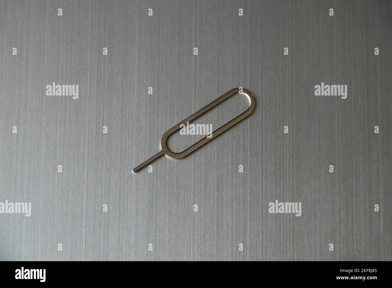 Der Clip zum Öffnen eines Steckplatzes für eine SIM-Karte liegt auf einem grauen Stahl Stockfoto