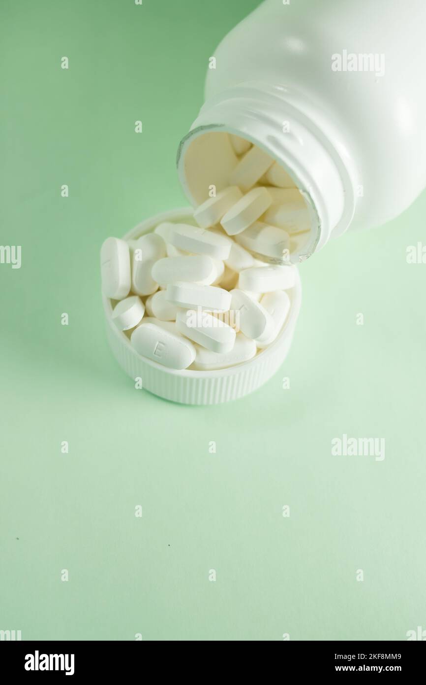 Ein Medizinglas und eine Kappe gefüllt mit Pillen auf grünem Hintergrund - Konzept der Gesundheit und Behandlung Stockfoto