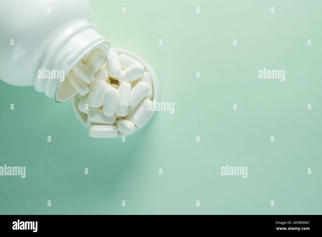 Eine Medikamentenflasche und eine Kappe gefüllt mit Pillen auf grünem Hintergrund - Konzept von Gesundheit und Behandlung Stockfoto