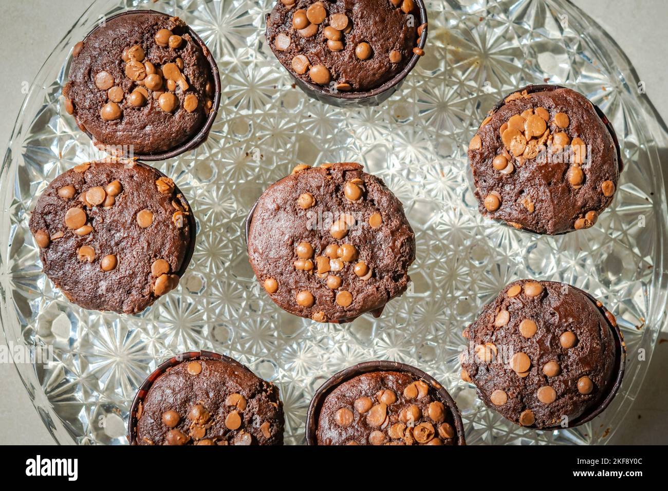Blick von oben auf hausgemachte Muffins mit Schokoladenkuchen auf einer Glasplatte. Direkt über der Nahaufnahme Makrofotografie mit seitlicher Sonneneinstrahlung. Stockfoto