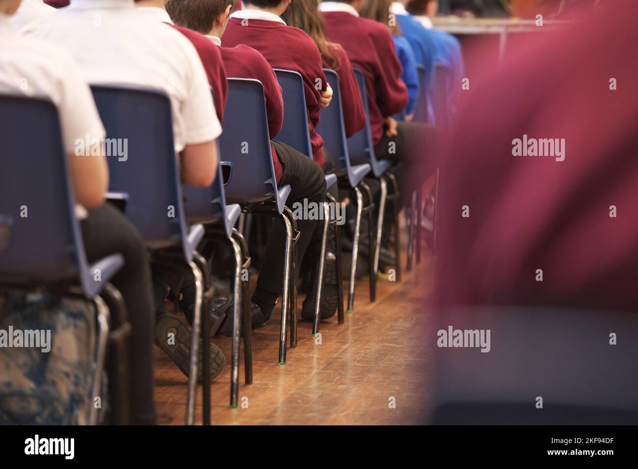 Junge Schüler sitzen in der Schulversammlung und hören dem Lehrer zu Stockfoto