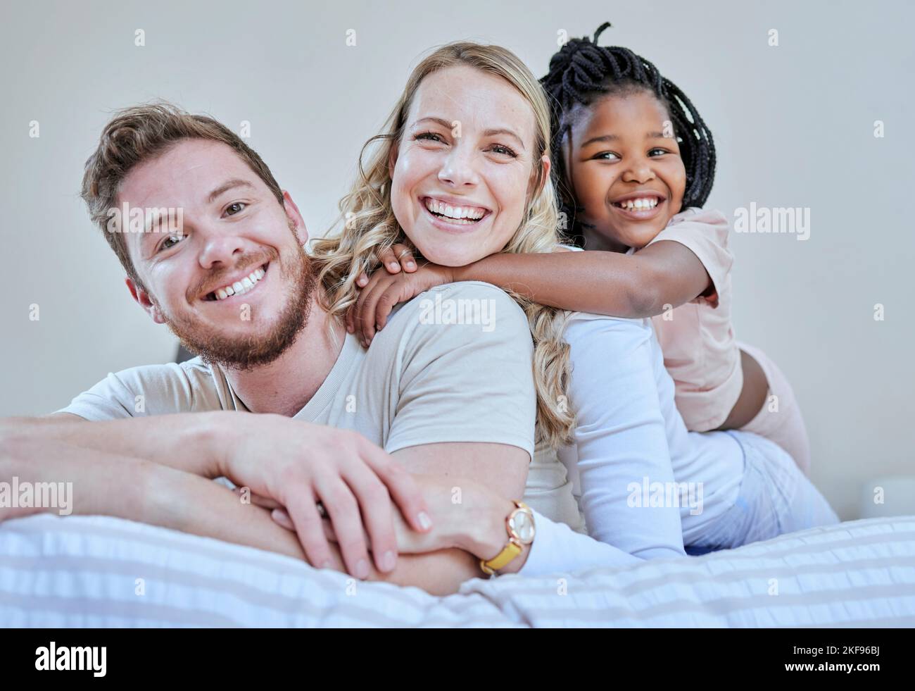 Familie, Eltern und Kind im interracial Portrait auf dem Bett mit Lächeln, Liebe oder glücklicher Bindung zu Hause. Schlafzimmer, multikulturelle Vielfalt und Stockfoto
