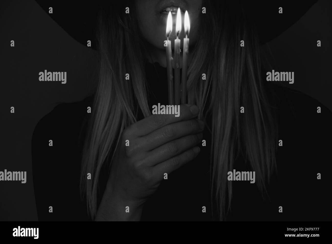 Ein Mädchen in einem schwarzen Hut im Dunkeln hält eine Kerze, ein Mädchen mit Kerzen in der Nacht Stockfoto