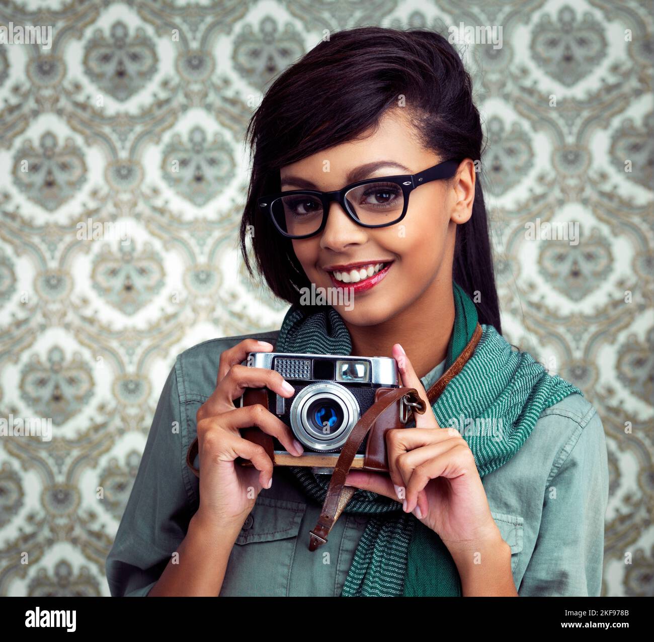 Jeden Moment festhalten. Eine junge Frau, die mit einer Kamera auf einem gemusterten Hintergrund posiert. Stockfoto