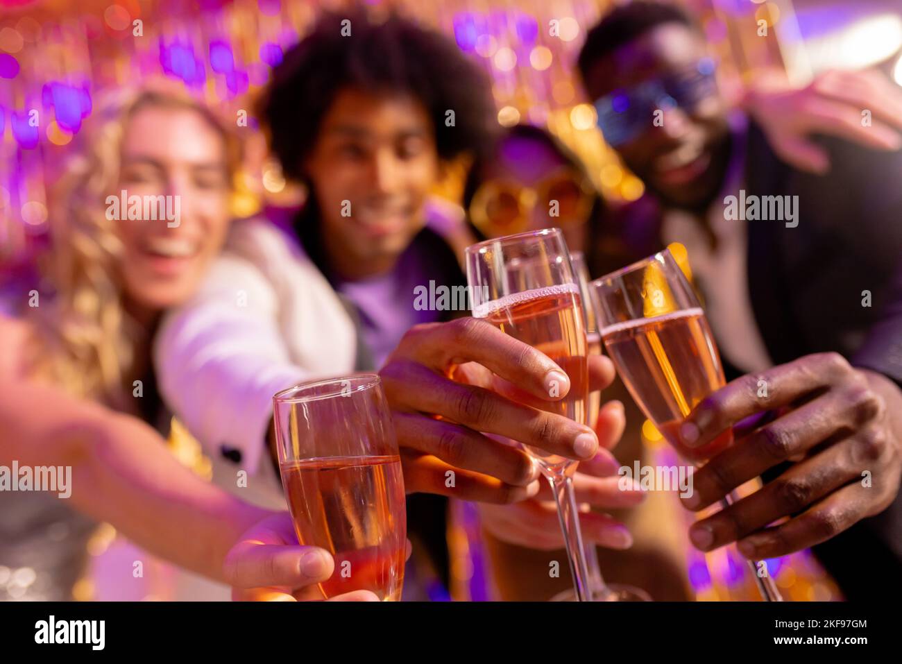 Selektiver Fokus von vier glücklichen, vielfältigen Freunden, die mit Gläsern Champagner in einem Nachtclub anstoßen Stockfoto