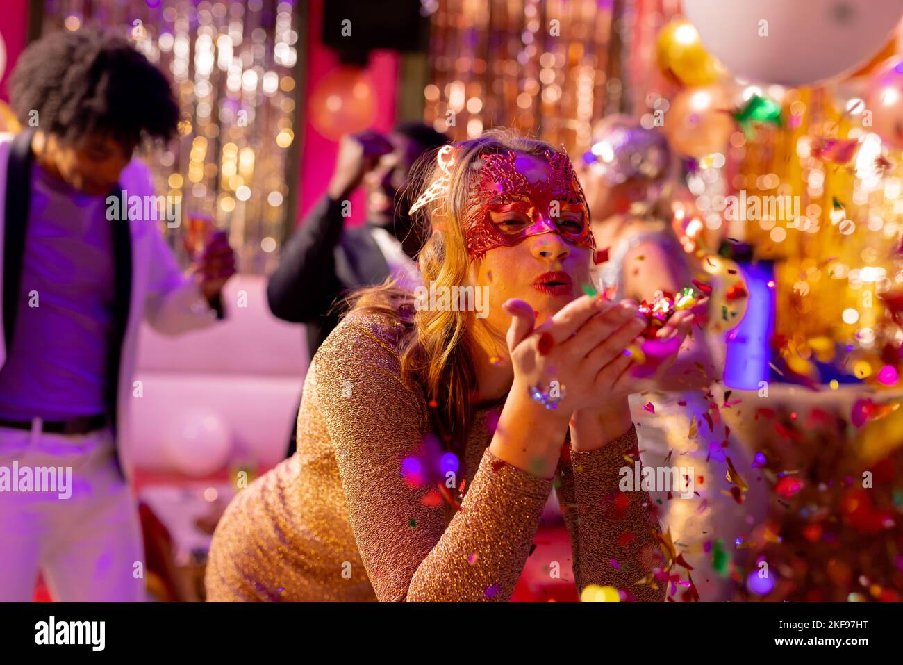Glückliche weiße Frau in Maske, die Glitzer auf der Tanzfläche bläst, auf einer Party in einem Nachtclub Stockfoto