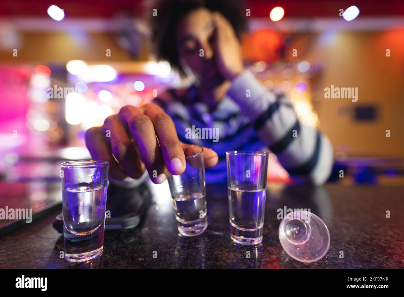 Betrunkener afroamerikanischer Mann sitzt an der Bar mit Schnapsgläsern, selektive Fokussierung Stockfoto