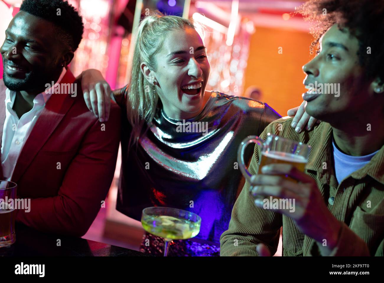 Glückliche Gruppe von verschiedenen männlichen und weiblichen Freunden, die an der Bar in einem Nachtclub trinken und sich unterhalten Stockfoto