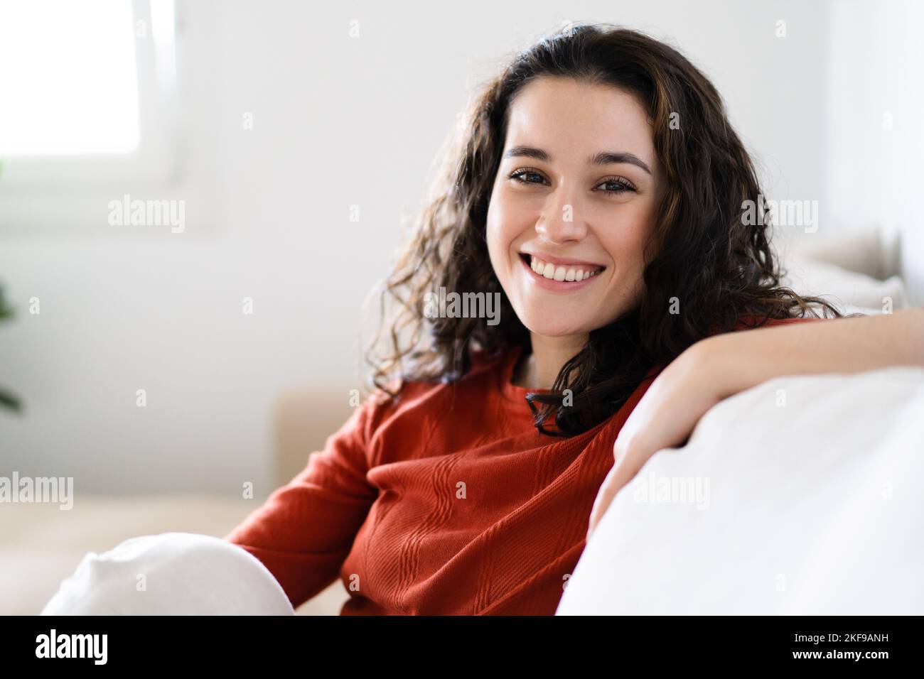 Junge schöne Brünette Frau lächelt vor der Kamera, während sie sich auf der Couch zu Hause ausruhen Stockfoto