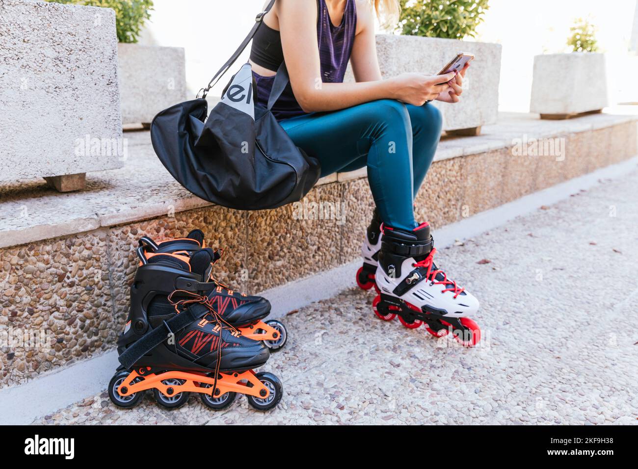 Unbekanntes junges Mädchen, das sich mit ihrem Mobiltelefon und ihrer Tasche auf Inline-Skates vorbereitet. Stockfoto