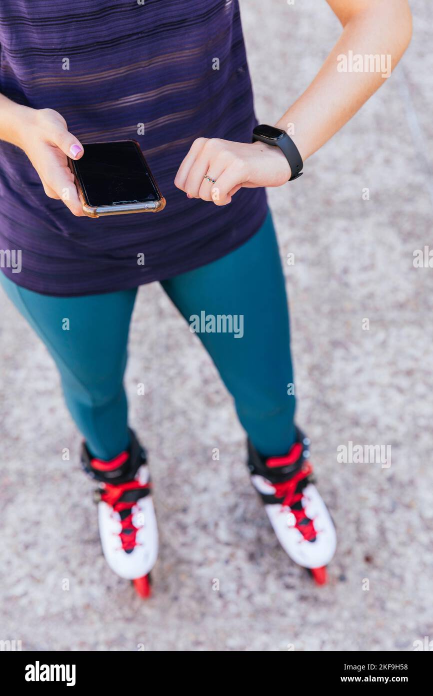 Unbekanntes junges Mädchen, das sich mit ihrem Mobiltelefon und ihrer Smartwatch auf Inline-Skates vorbereitet. Stockfoto