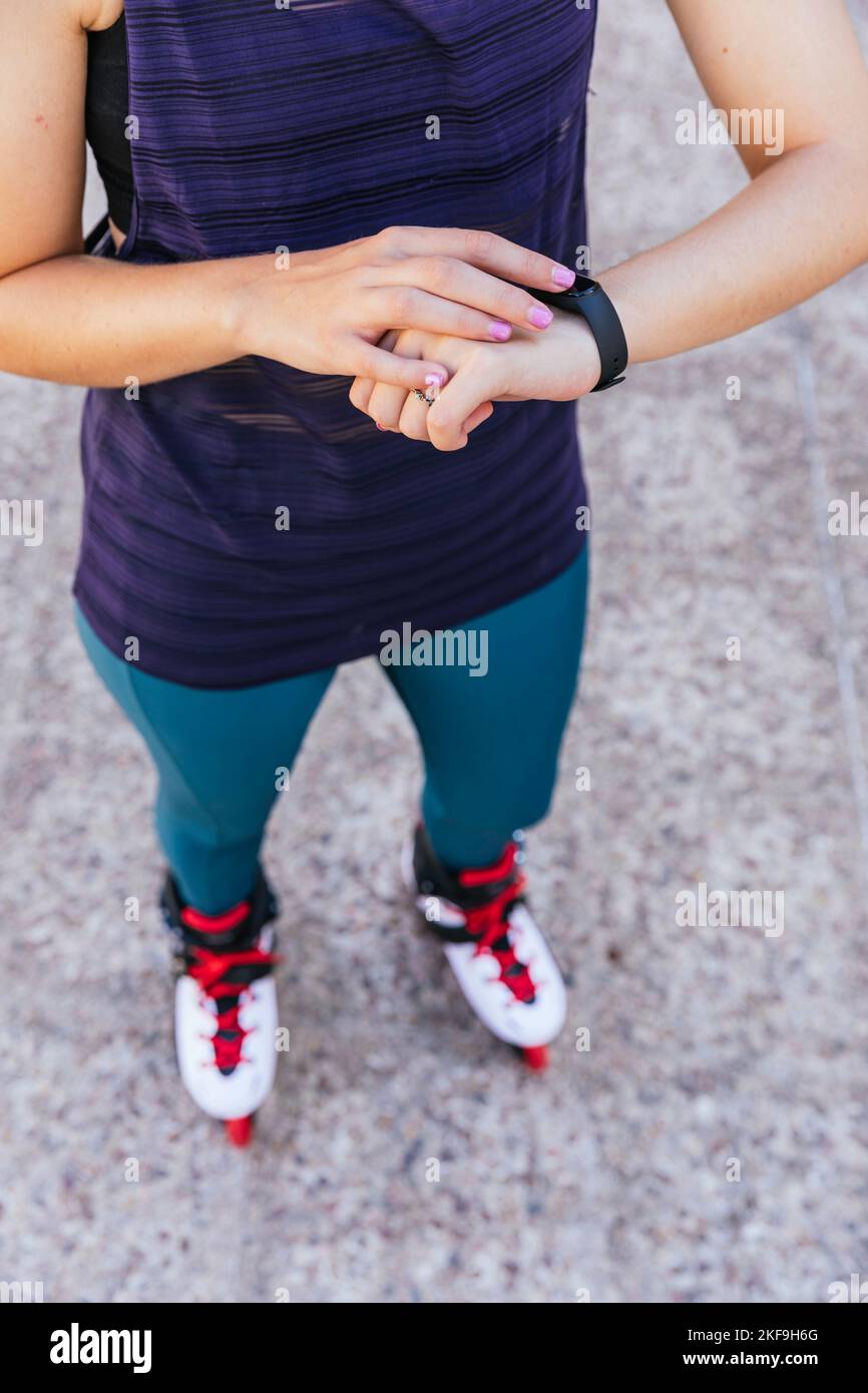 Unbekanntes junges Mädchen, das sich auf ihrer Smartwatch bereit macht, auf Inline-Skates zu gehen Stockfoto