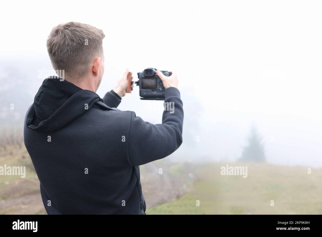 Junger männlicher Fotograf auf nebliger Wiese, der Fotos machte. Stockfoto
