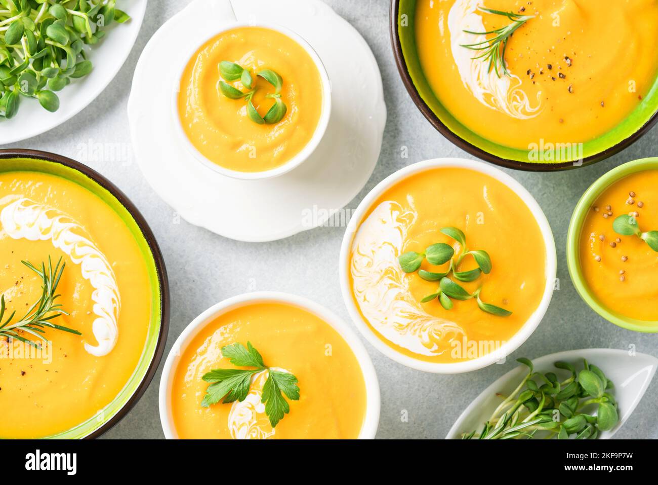 Viele Schüsseln mit cremiger Kürbis-Fallsuppe auf dem hellgrauen Tisch ...