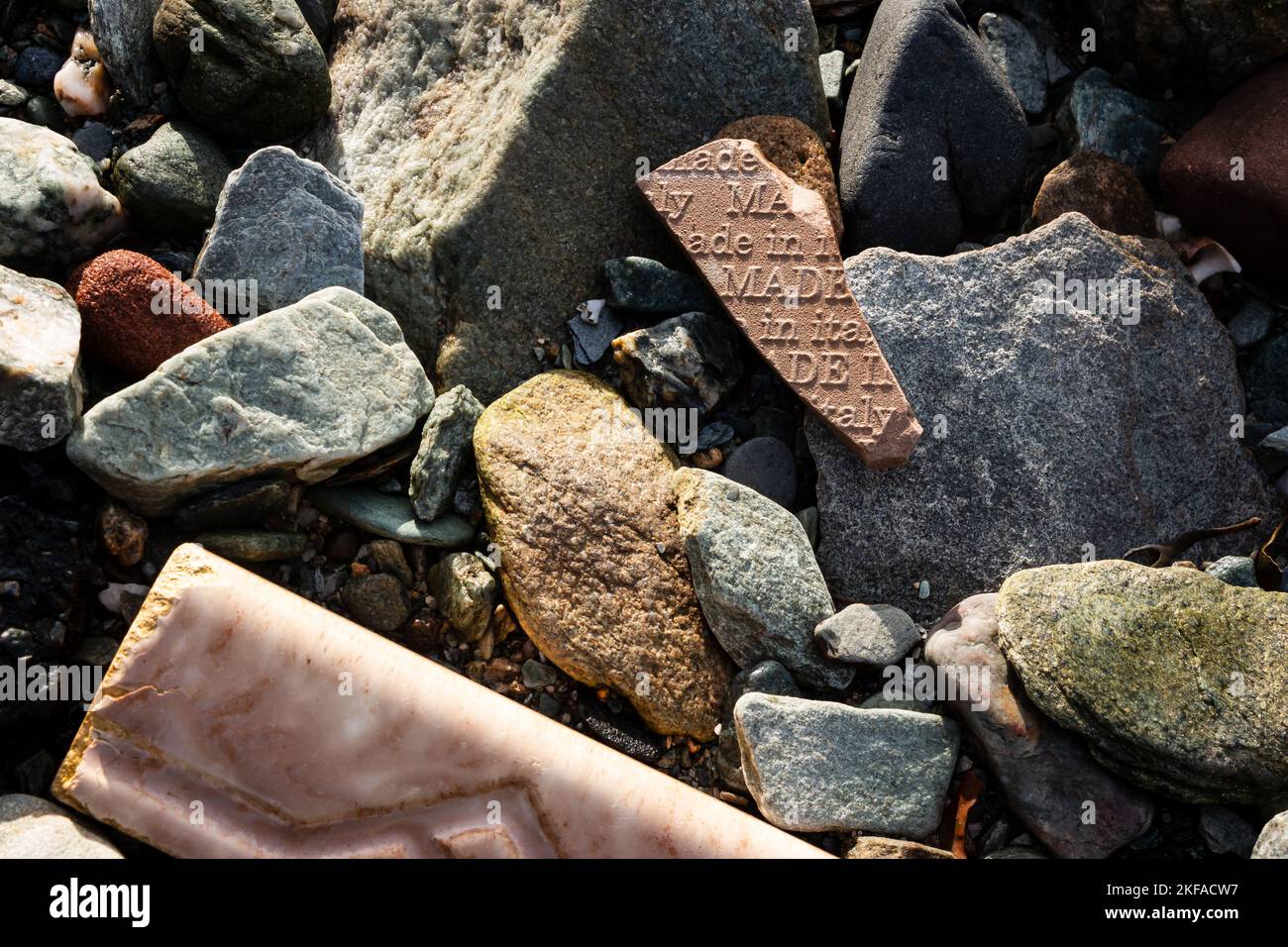 Nahaufnahme von Steinen und Trümmern am Strand mit einem Keramikfragment, das sagt: „Made in Italy“ Stockfoto