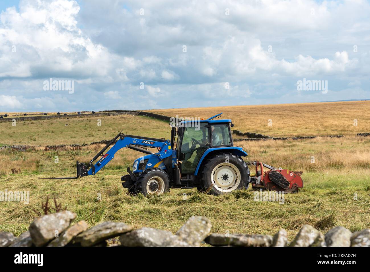 Aufgenommen am 31. August 2022, Slaidburn, Clitheroe, Lancashire UK. Bauer schneidet sein Grasfeld in seinem blauen Traktor. Grüne Felder und sonniger blauer Himmel. Stockfoto