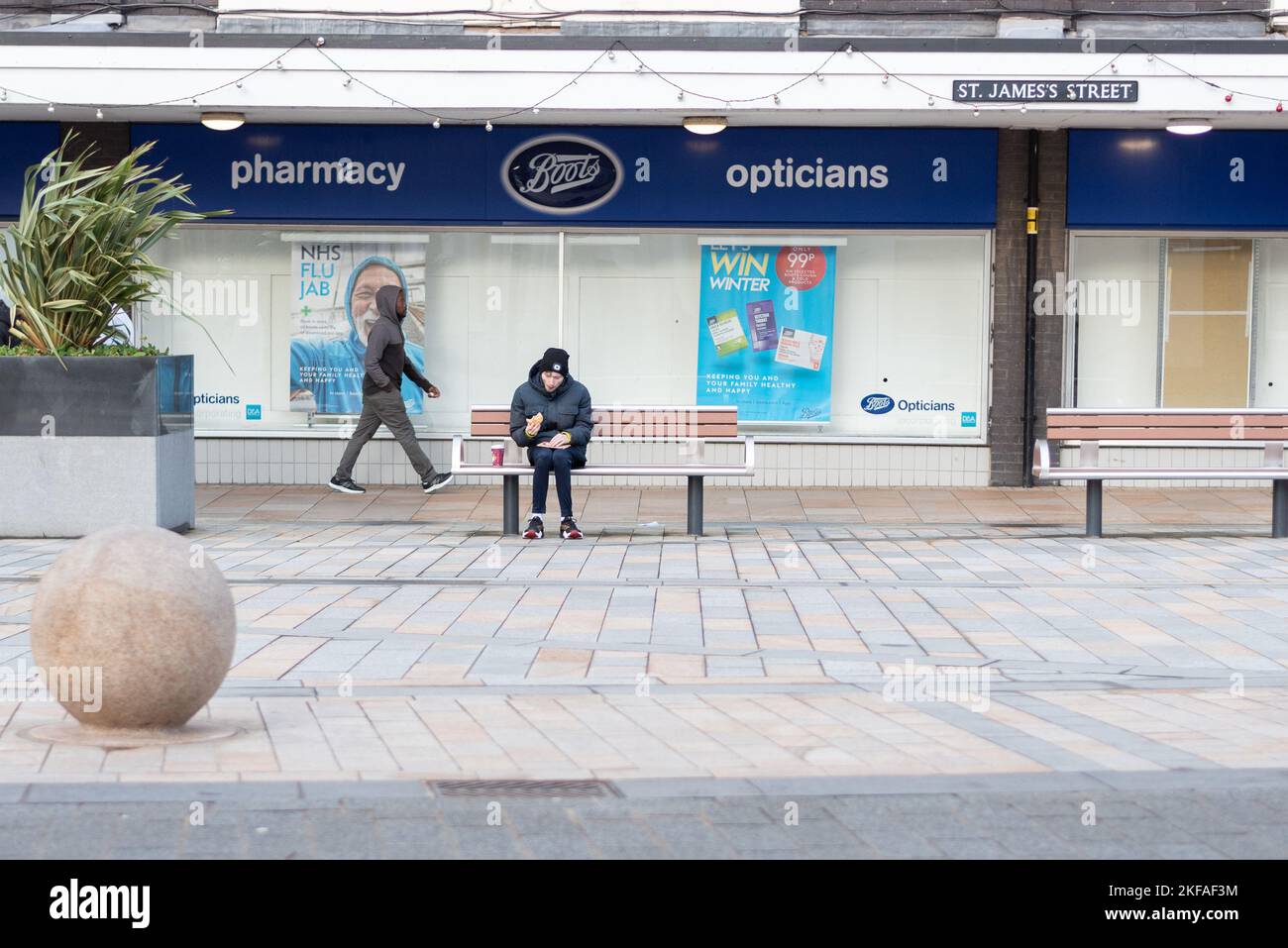 Der Junge, der eine Mahlzeit aß, saß auf einer Bank vor der Apotheke Boots im Stadtzentrum von Burnley. Stockfoto