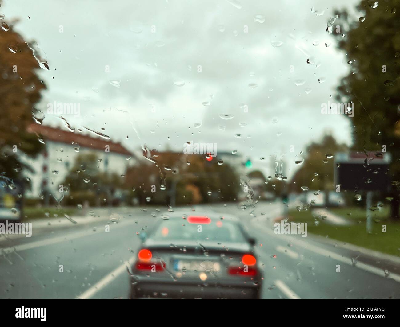 Regen, Regen fällt auf das Fenster eines Autos über der Straße mit Verkehr an einem regnerischen Tag. Fahrzeuge auf der Straße sichtbar von hinten Regentropfen auf der Windschutzscheibe eines Autos Stockfoto