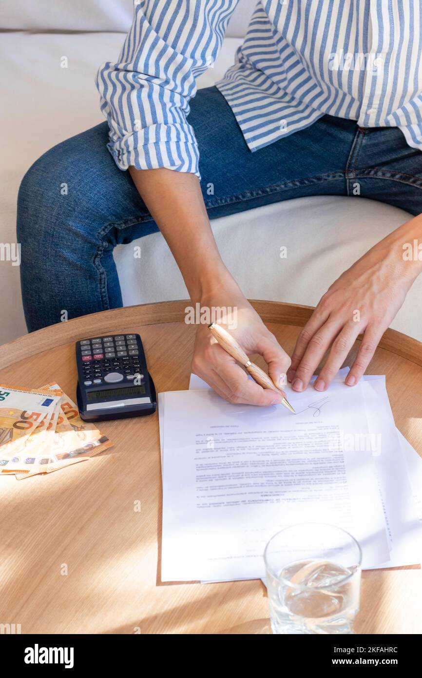 Vertikale Ansicht eines nicht erkennbaren Mannes, der das Vertragsdokument mit einem Stift auf einem Holztisch unterschrieb. Rechner, Geldscheine in Euro Währung um Stockfoto