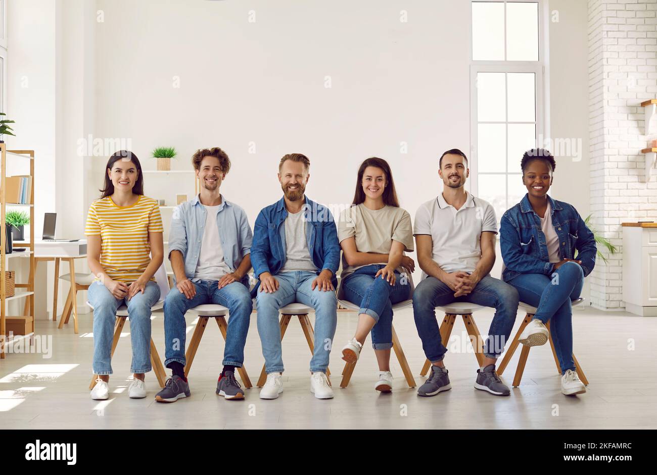 Porträt lächelnder, multirassischer junger Menschen in legerer Kleidung, die in Reihe auf Stühlen sitzen. Stockfoto