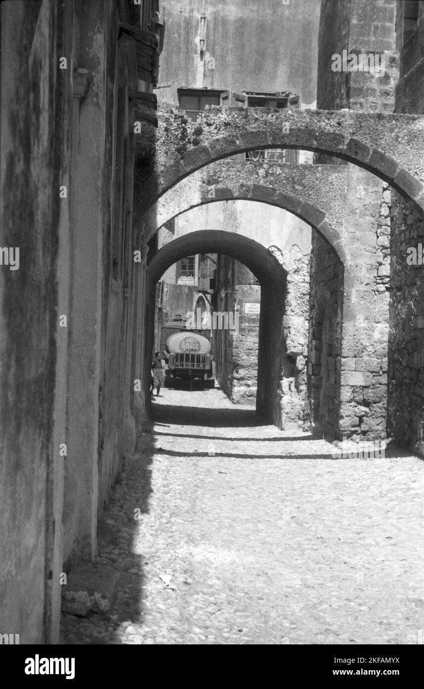 Eine kleine menschenleere Gasse im Sonnenschein in Griechenland im Hintergrund ein Shell Tankwagen, 1950er Jahre. Eine kleine verlassene Gasse im Sonnenschein in Griechenland im Hintergrund ein Shell-Tanker, 1950s. Stockfoto