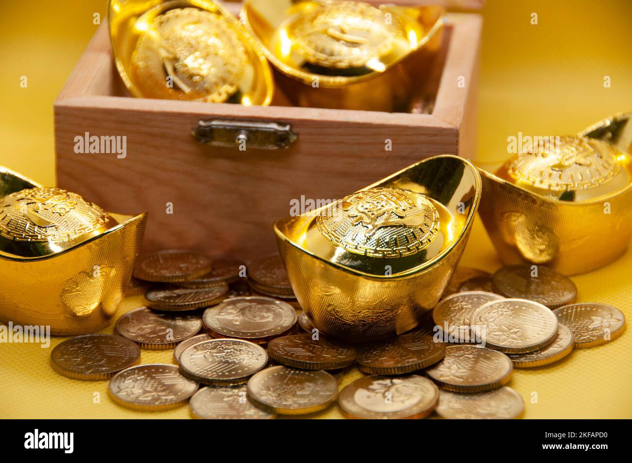 Chinesische Goldbarren und Münzen in Schatzkiste auf gelbem Hintergrund. Wohlstandskonzept. Stockfoto