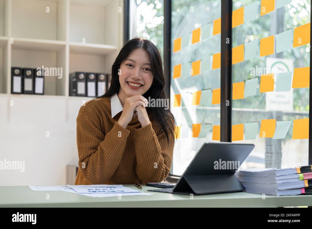 Porträt einer jungen, schönen asiatischen Geschäftsfrau, die am Laptop sitzt und lächelt und die Kamera anschaut Stockfoto
