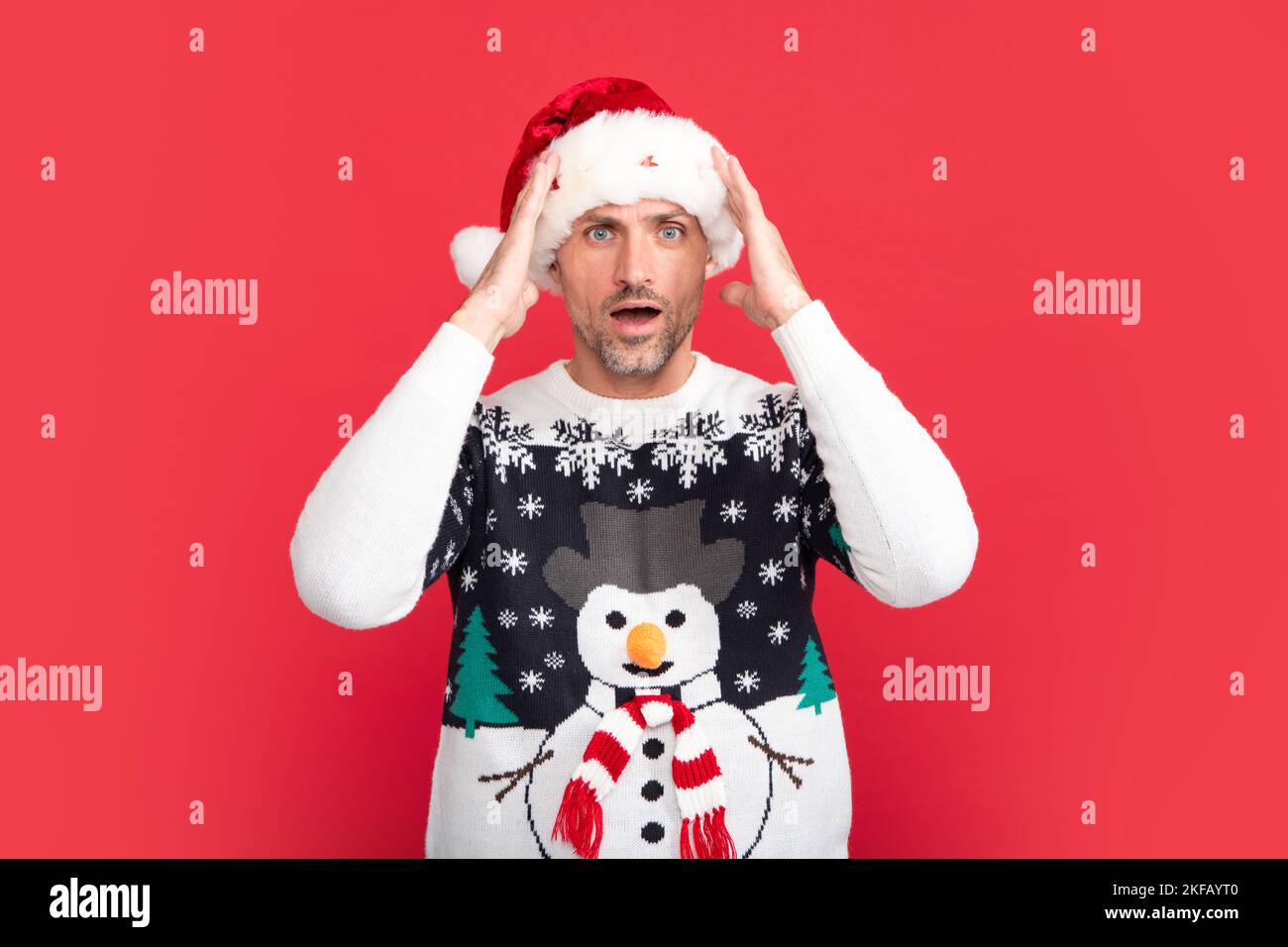 Studio Portrait von Kerl trägt weihnachtsmann Hut und Winter Pullover. Mann mit weihnachtshut auf isoliertem rotem Hintergrund. Stockfoto