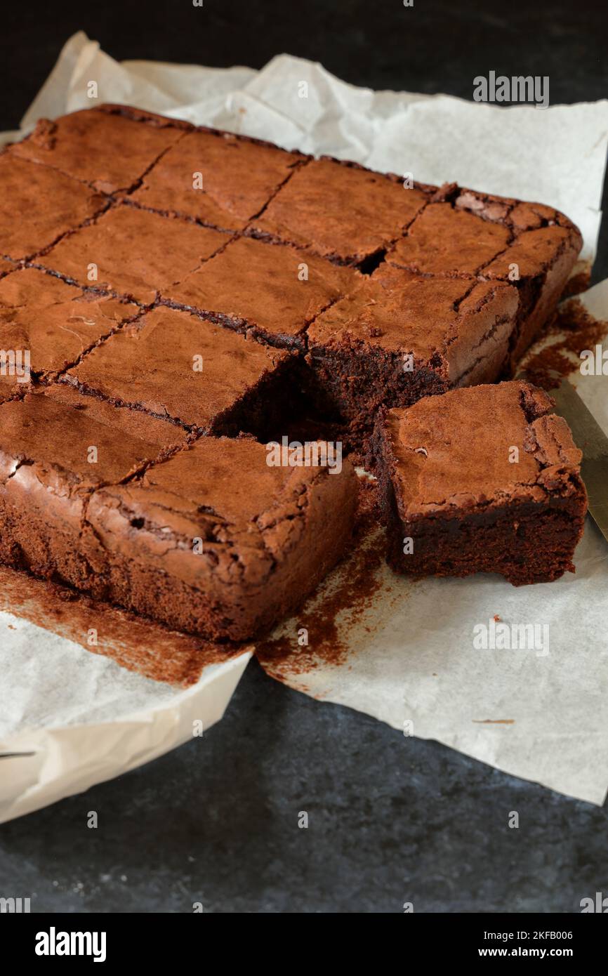 Hausgemachte, leckere Schokoladenbrownies, frisch aus dem Ofen, in Quadrate geschnitten und mit Backpapier abgeschält. Sehr geringe Schärfentiefe Stockfoto