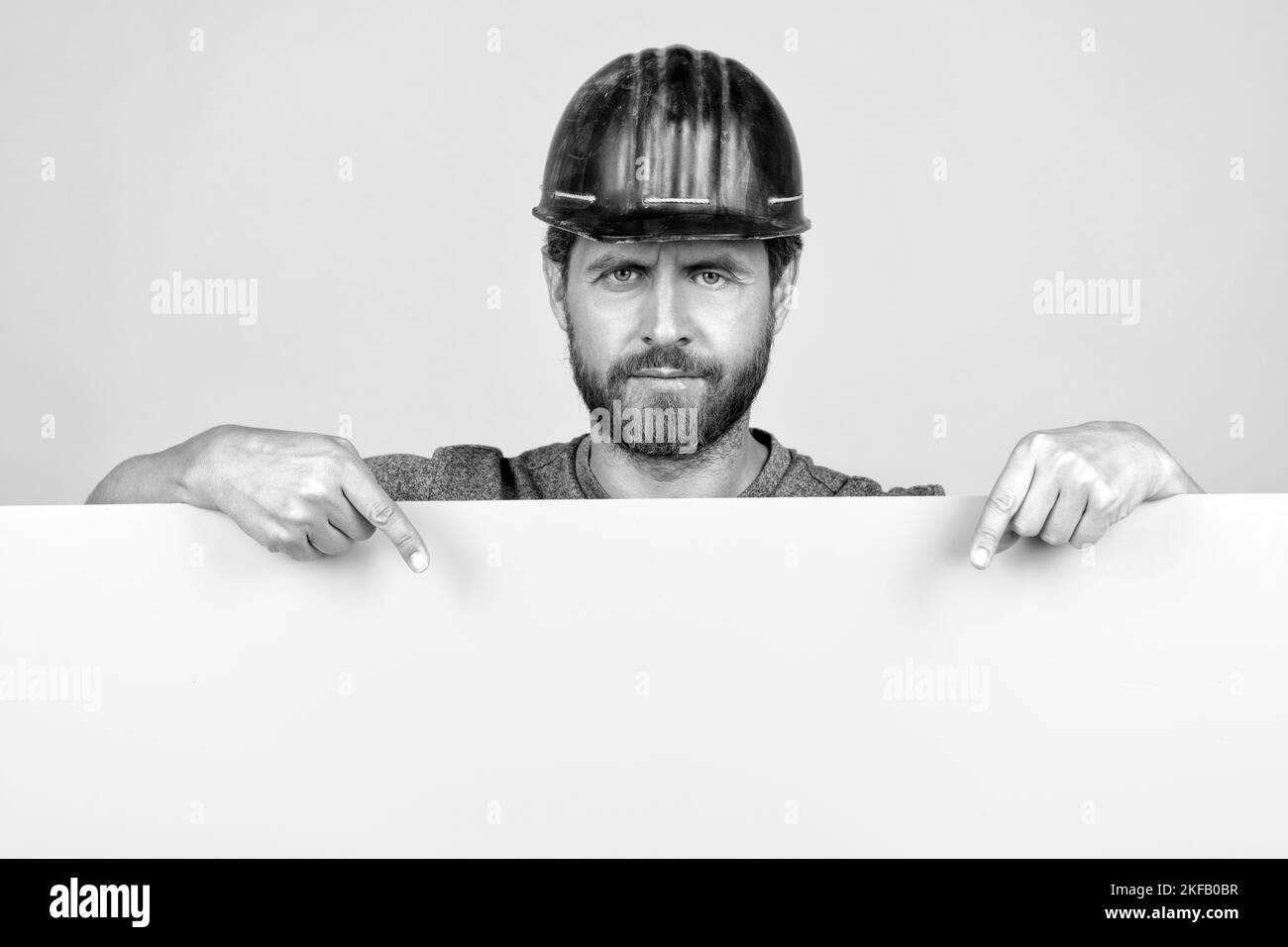 Reifer Mann Arbeiter im Helm zeigt Finger auf gelbem Papier für Kopierraum, Ankündigung Stockfoto