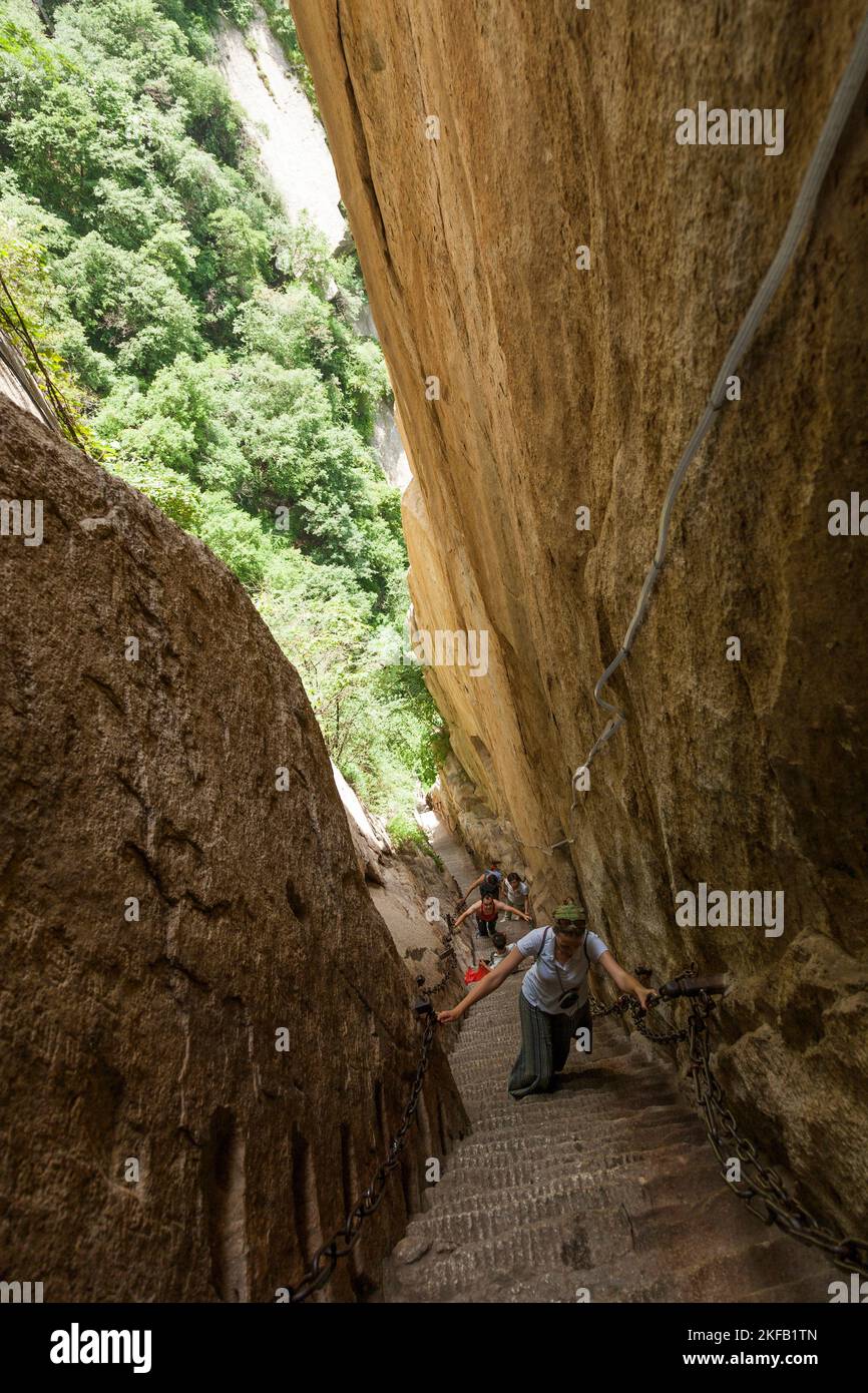 Eine westeuropäische Touristin klettert steile Stufen hoch, die in den Steinboden eines schmalen Passes auf dem Huashan Mountain / Mount Hua / Mt Hua in der Nähe von Huayin, Weinan, China, VR China gehauen und geschnitzt wurden. (125) Stockfoto