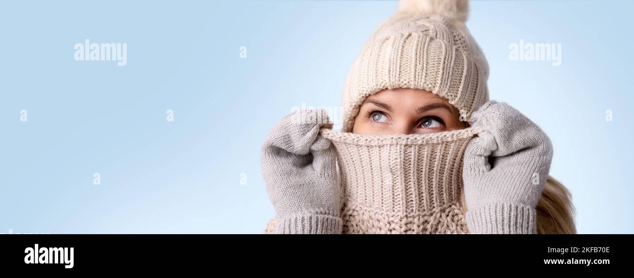 Frau in gestrickten Wollkleidung versteckt ihr Gesicht in Pullover und suchen isoliert auf blauem Hintergrund. Wintermode. Warme Kleidung. Banner mit Kopie s Stockfoto