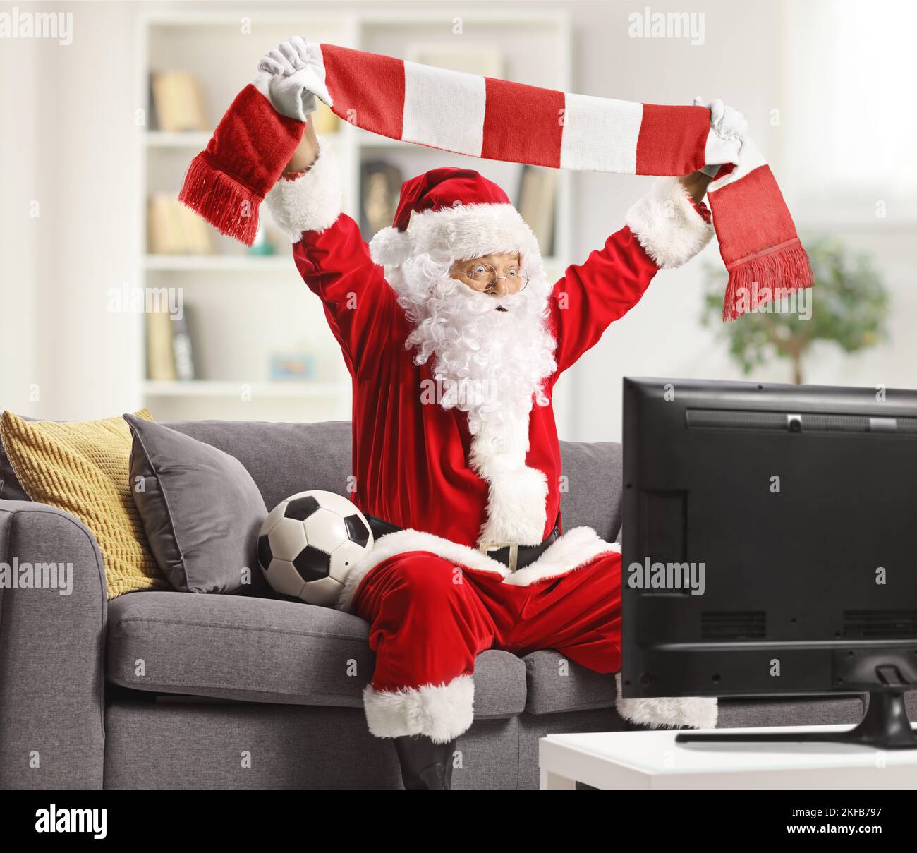 Aufgeregter weihnachtsmann, der Fußball im fernsehen sieht und zu Hause mit einem Schal jubelt Stockfoto