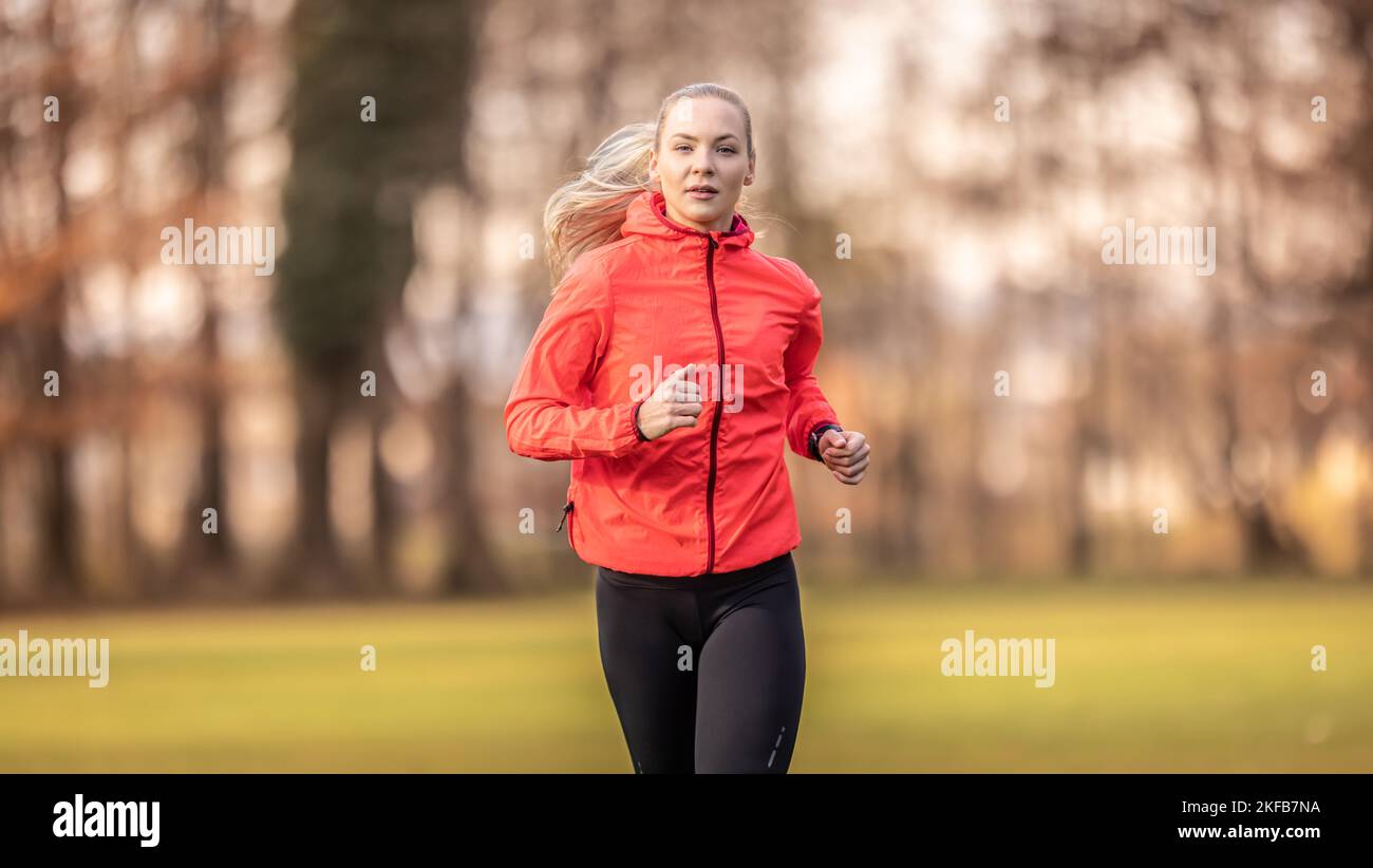 Eine schöne junge Blondine in Sportswear trainiert im Park fürs Laufen. Stockfoto