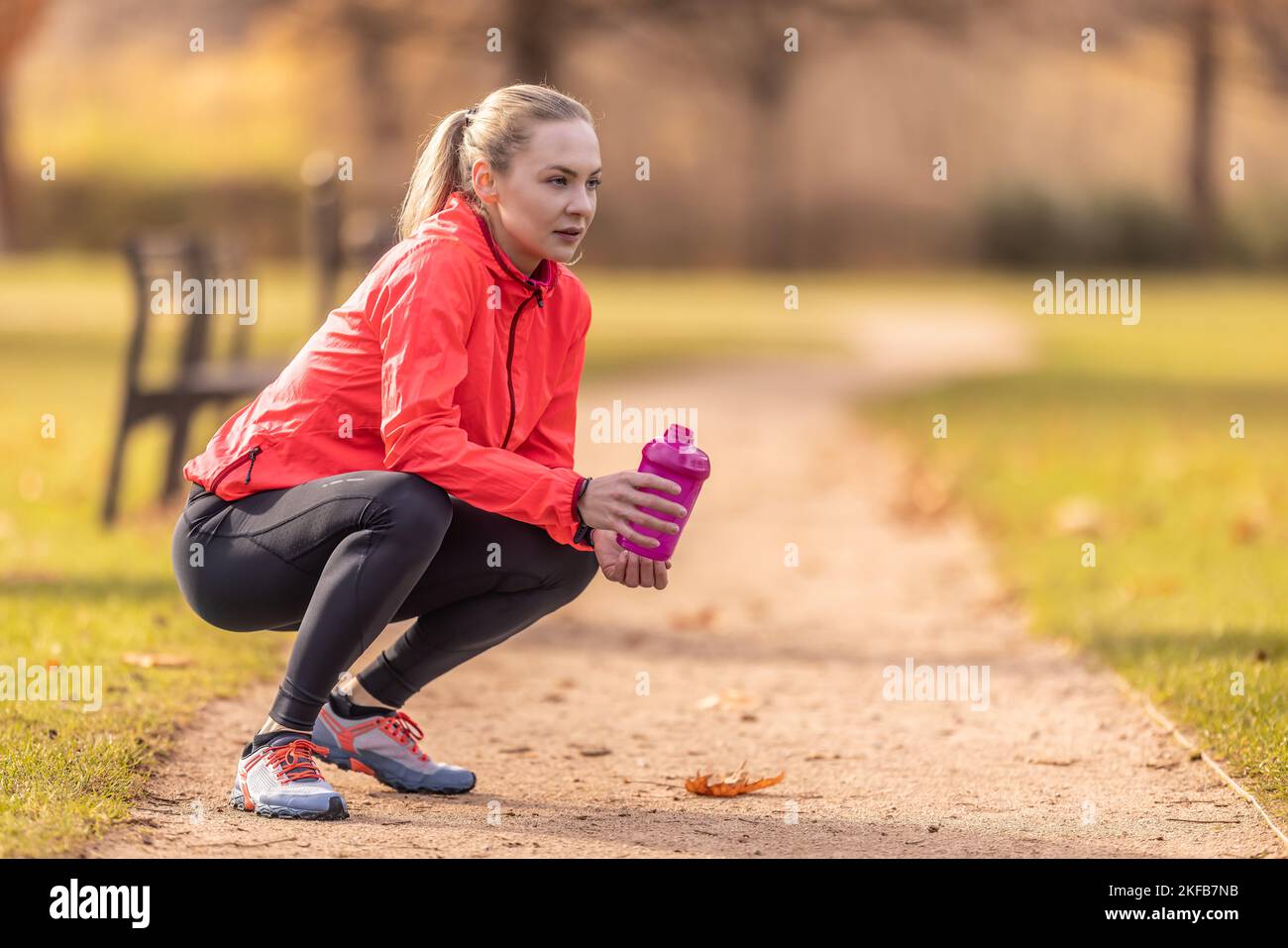 Eine ruhende Sportlerin hält eine Plastikflasche mit einem Getränk in der Hand, nachdem sie im Park gelaufen ist. Stockfoto