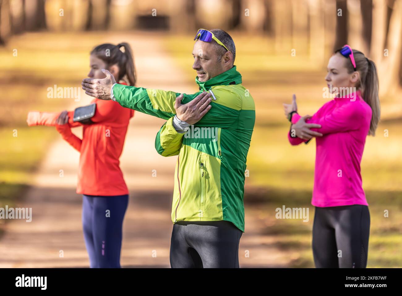 Drei Amateursportler reifen Mann und zwei junge Frauen wärmen sich vor dem Joggen auf und machen Oberkörper-Stretching im Park. Stockfoto